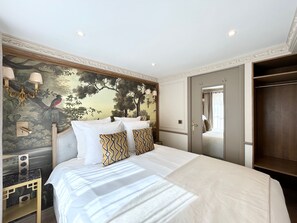 A hotel room with a large bed, a wardrobe, a vanity with a mirror, and a wall with a nature-themed mural.