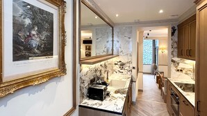 A modern kitchen with marble countertops, a sink, and a toaster. There is a framed artwork on the wall and a mirror above the sink. - Merveil - Signature Suite - Tour Eiffel - Bourgogne (Paris)
