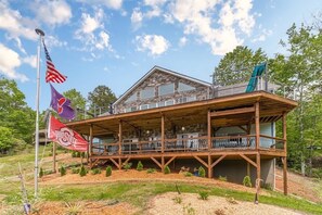 A two-story wooden building with a balcony, surrounded by trees and a flagpole with flags.