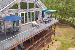 A multi-level stone building with a covered deck, outdoor seating, and a view of the surrounding forest. - HOUSE OF BLUES | LUXURY GOLF/MOUNTAIN RETREAT (Helen)