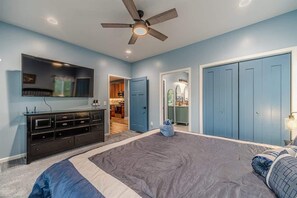 A bedroom with a bed, a ceiling fan, a dresser, and a TV mounted on the wall.