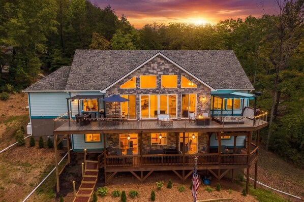 A two-story house with a stone facade, large windows, and a deck with outdoor seating.