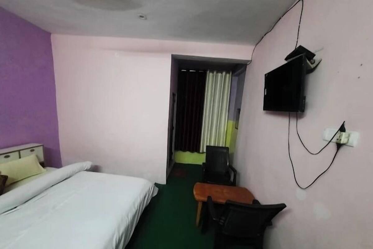 A hotel room with a bed, a desk, a chair, a TV mounted on the wall, and a window with curtains.