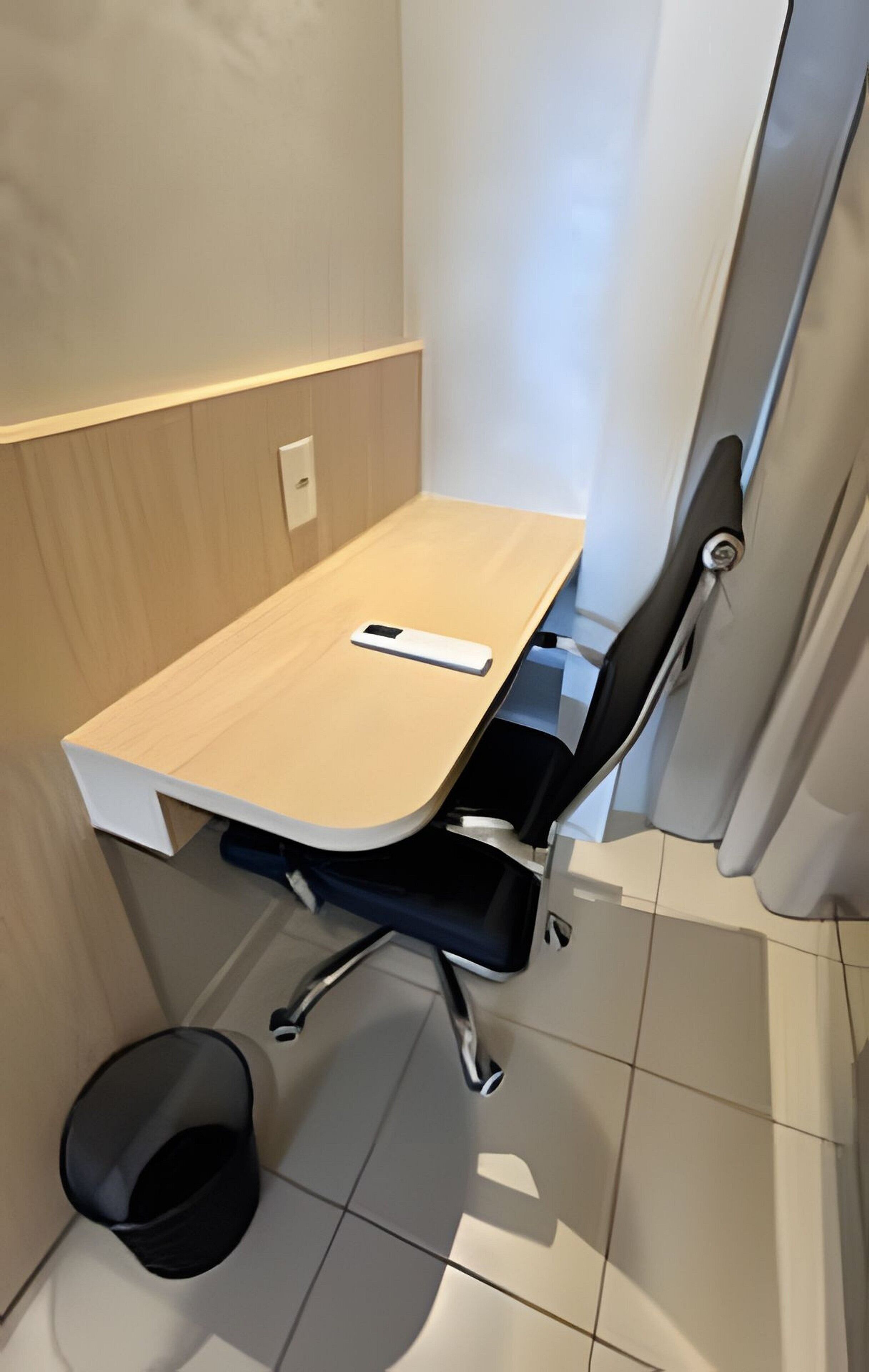 A small, modern bathroom with a wooden vanity, a black chair, and a white bucket.