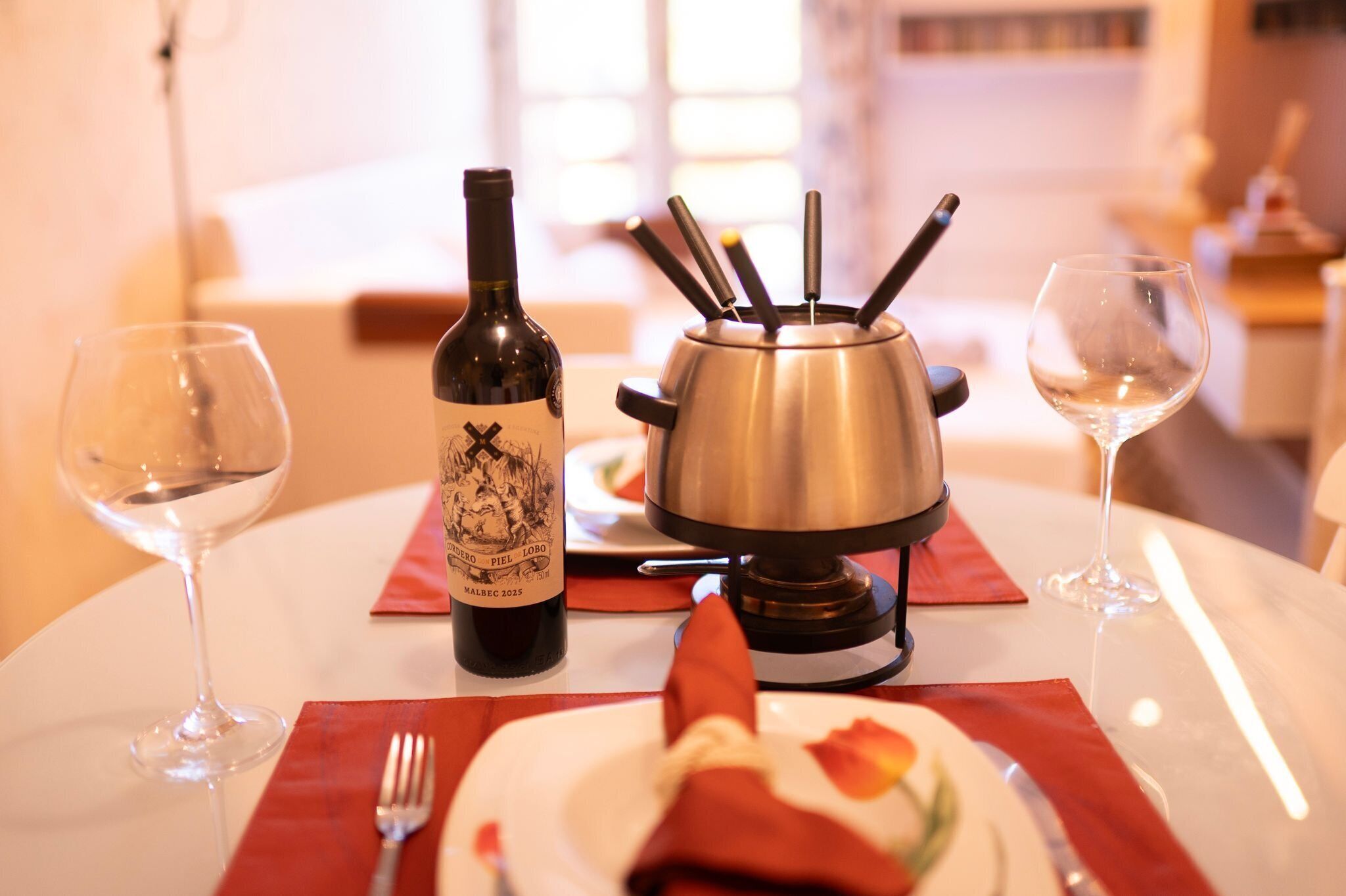 A dining table with a bottle of wine, a hot plate, and two empty wine glasses.