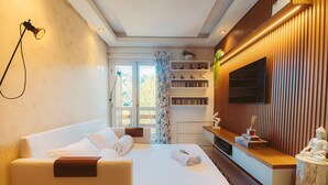 A modern hotel room with a bed, bedside table, TV, and a view of the outdoors. - Apto no Coração do Capivari e Perto de Tudo! (Campos do Jordão)