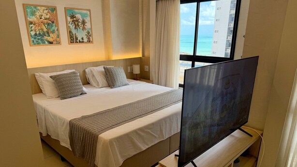 Ett hotellrum med en säng, en tv på ett stativ och ett fönster med utsikt över havet.