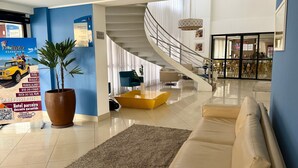En modern hotellobby med en trappa, en sittgrupp och en stor krukväxt.