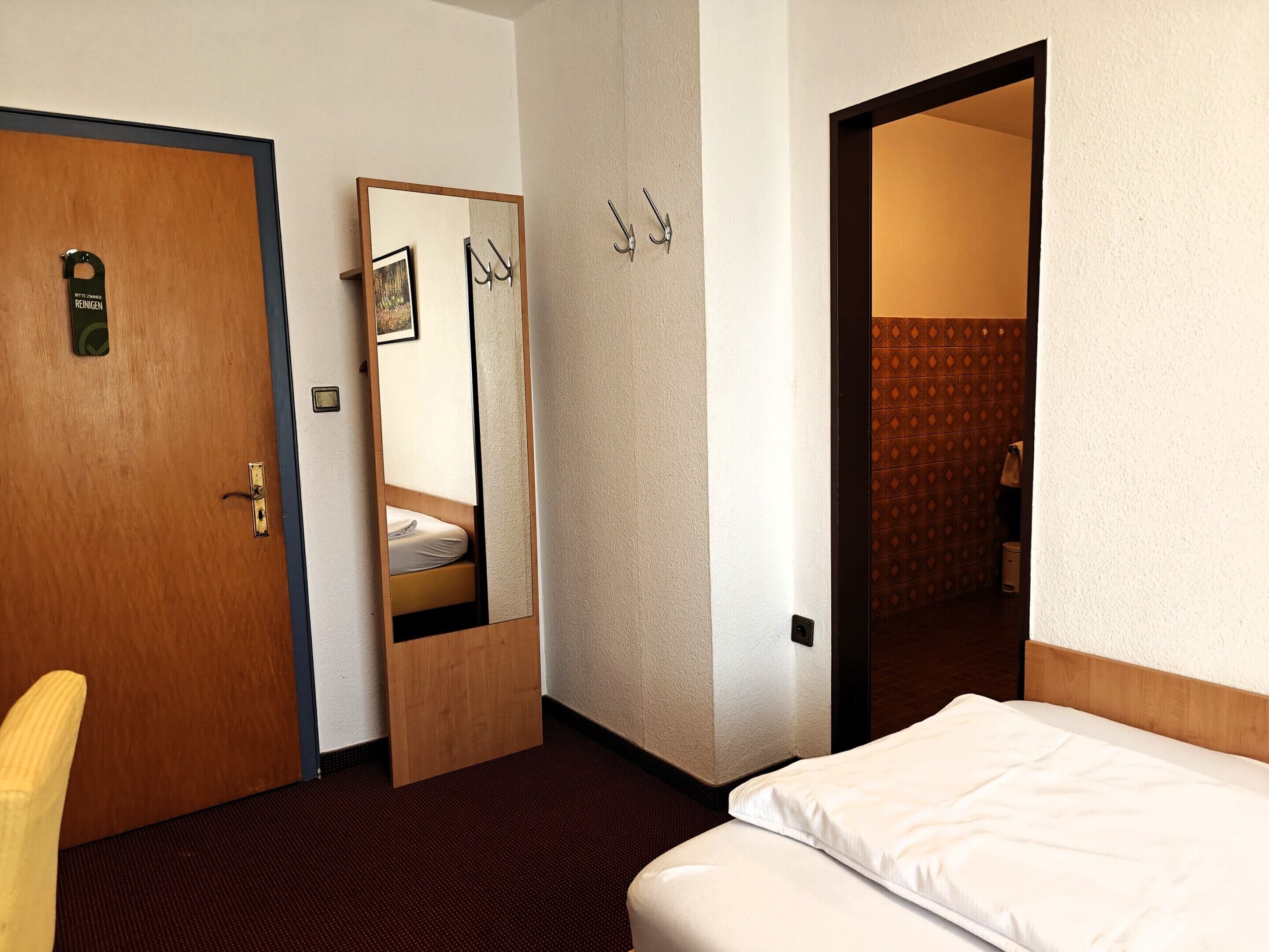 Una habitación de hotel con una cama, una puerta de madera, un espejo y un perchero.