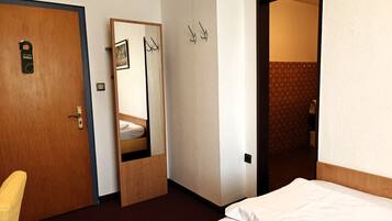 Una habitación de hotel con una cama, una puerta de madera, un espejo y un perchero.