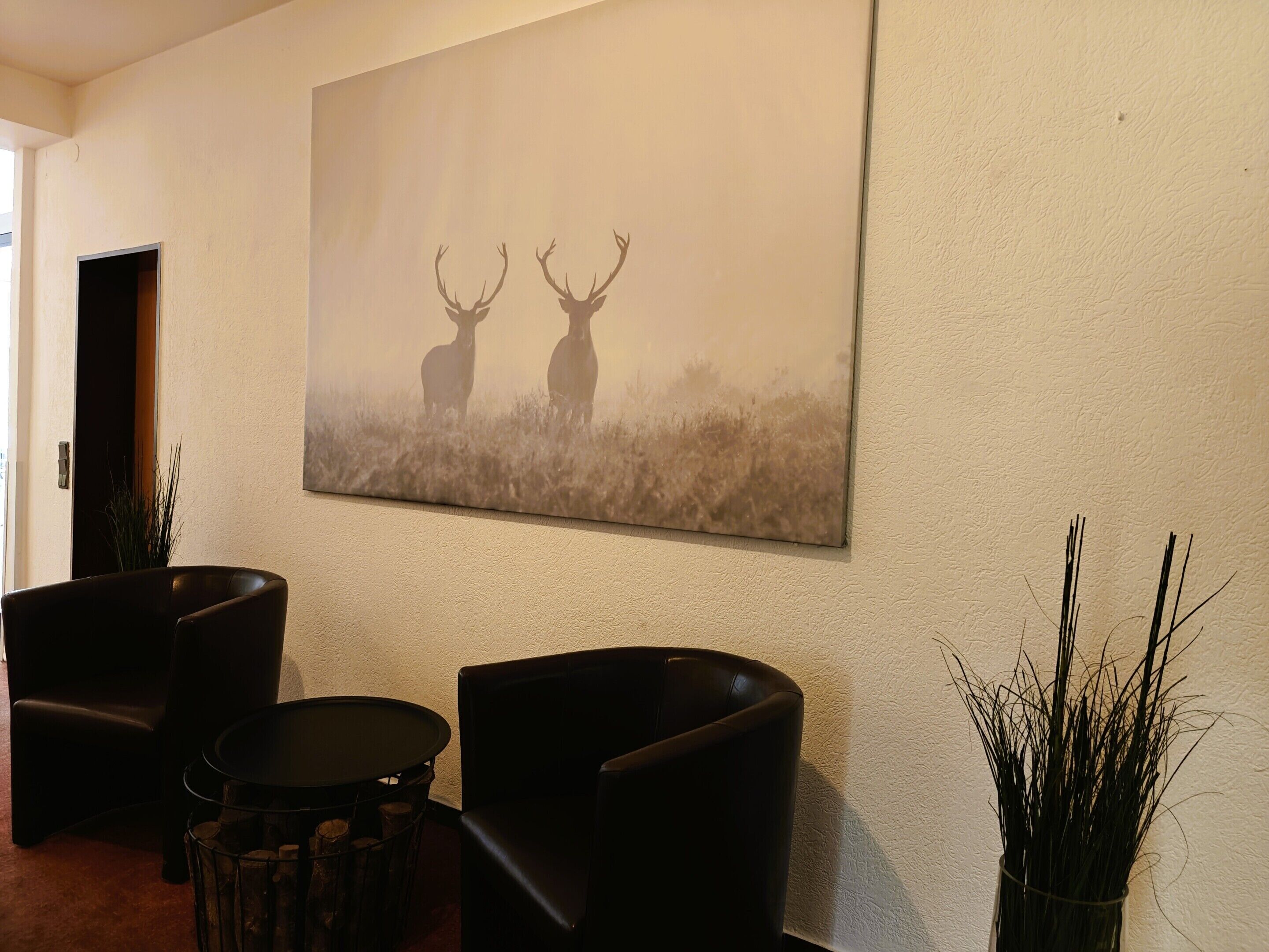 Une pièce comprenant un grand tableau représentant un cerf, accroché au mur, deux fauteuils en cuir, une petite table ronde et une plante en pot.