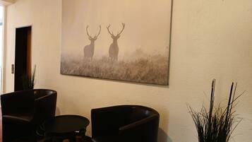 Une pièce comprenant un grand tableau représentant un cerf, accroché au mur, deux fauteuils en cuir, une petite table ronde et une plante en pot.