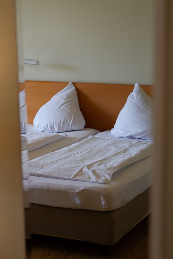 Una cama con ropa de cama y almohadas blancas, un cabecero de madera y una pared lisa.