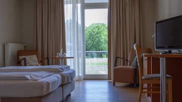 Habitación de hotel con cama, dos sillas, escritorio con televisor y balcón con cortinas.