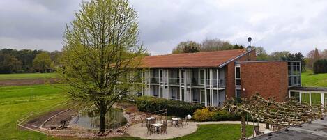 A modern building with a brick facade and large windows. There is a circular patio area with outdoor seating and a small pond.