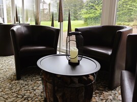 A cozy seating area with two dark leather chairs and a round table with a candle in a wire holder.