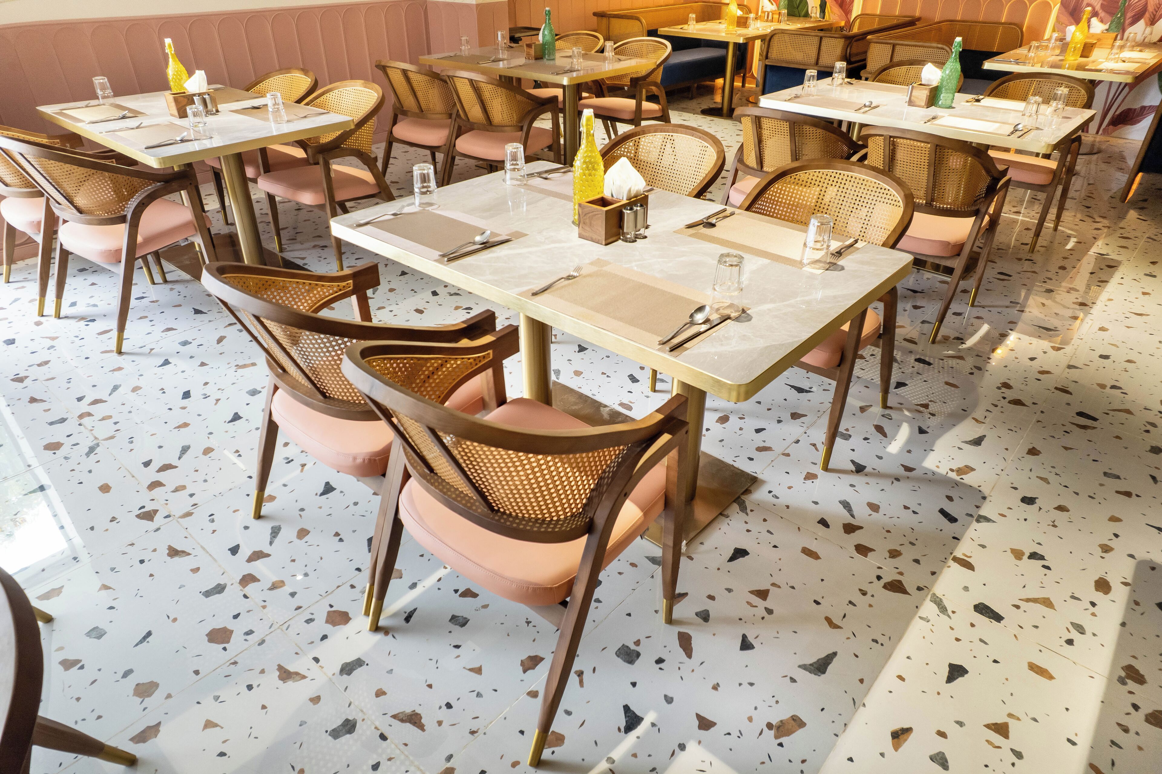 A restaurant interior with round tables, wicker chairs, and a terrazzo floor.