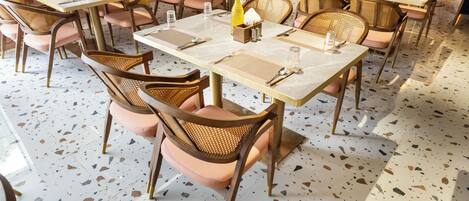 A restaurant interior with round tables, wicker chairs, and a terrazzo floor.