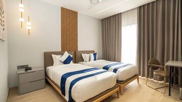 A hotel room with two beds, a desk, a chair, a ceiling fan, and a nightstand.