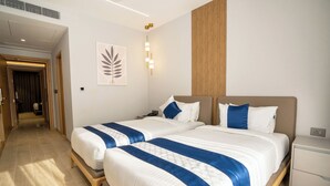 A hotel room with two beds, a wooden bench, a nightstand, and a wall-mounted light fixture. - Trunk & Trolley A Luxury Boutique Hotel  (Hyderabad)