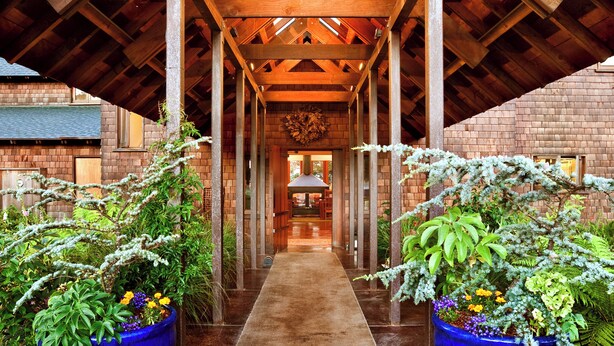 A covered walkway with wooden beams and brick walls, leading to a central area with a fireplace. - Cozy Loft with Ocean Views @Brewery Gulch INN (Mendocino)