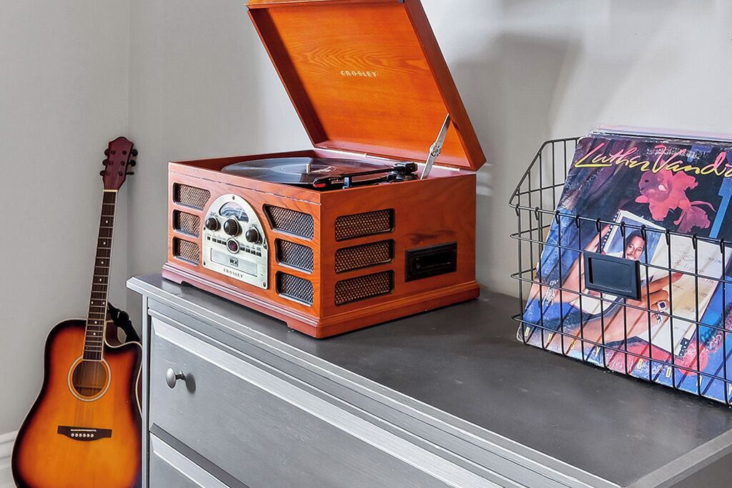 Une platine vinyle en bois posée sur une commode, une guitare et une affiche encadrée.