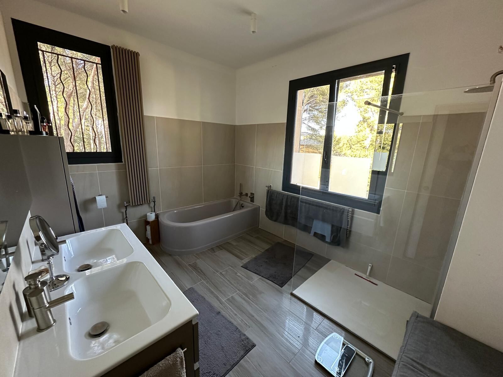 A modern bathroom with a bathtub, two sinks, and a large window providing natural light.