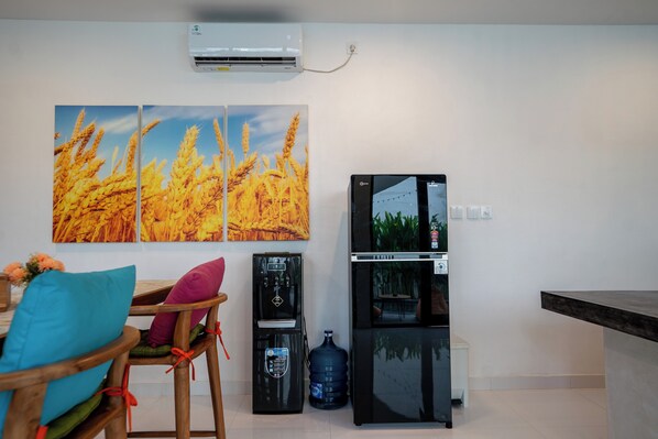 A modern kitchen with a black refrigerator, water dispenser, and a large water jug. There are two chairs with colorful cushions and a table with a vase of flowers.