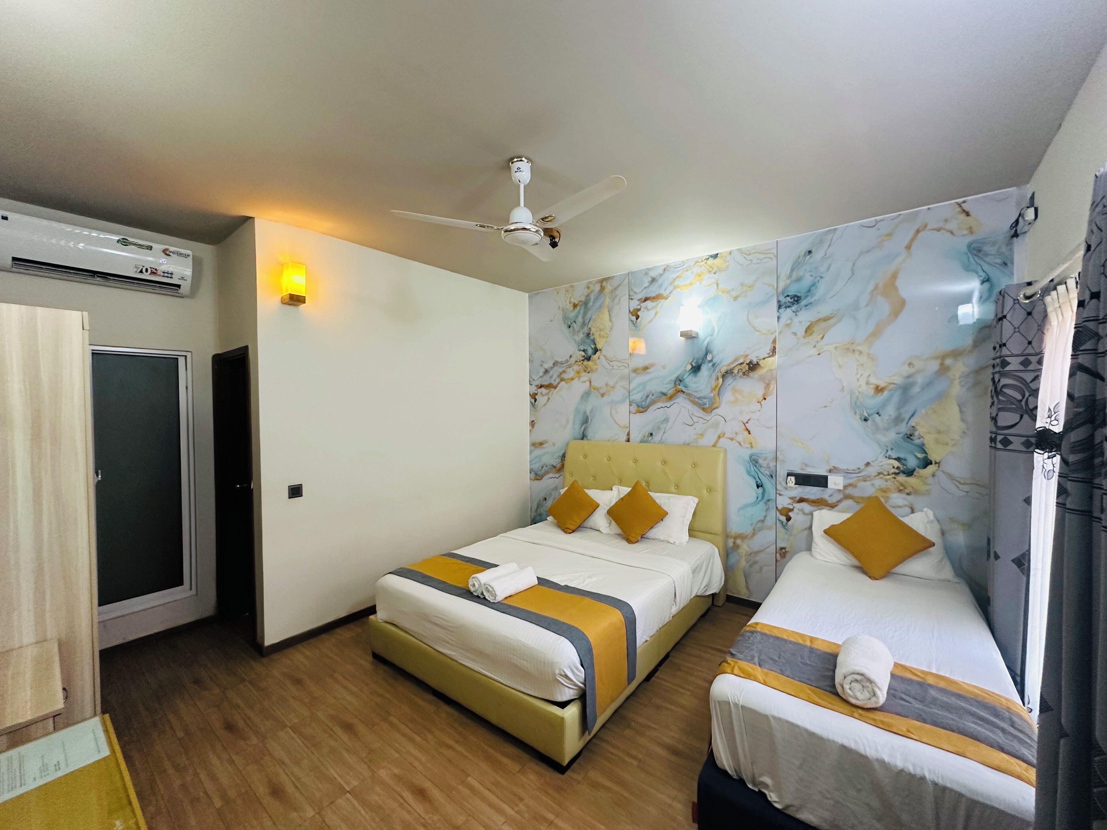 Ein Hotelzimmer mit zwei Betten, einem Deckenventilator, einer Klimaanlage und Wänden mit Marmoroptik.