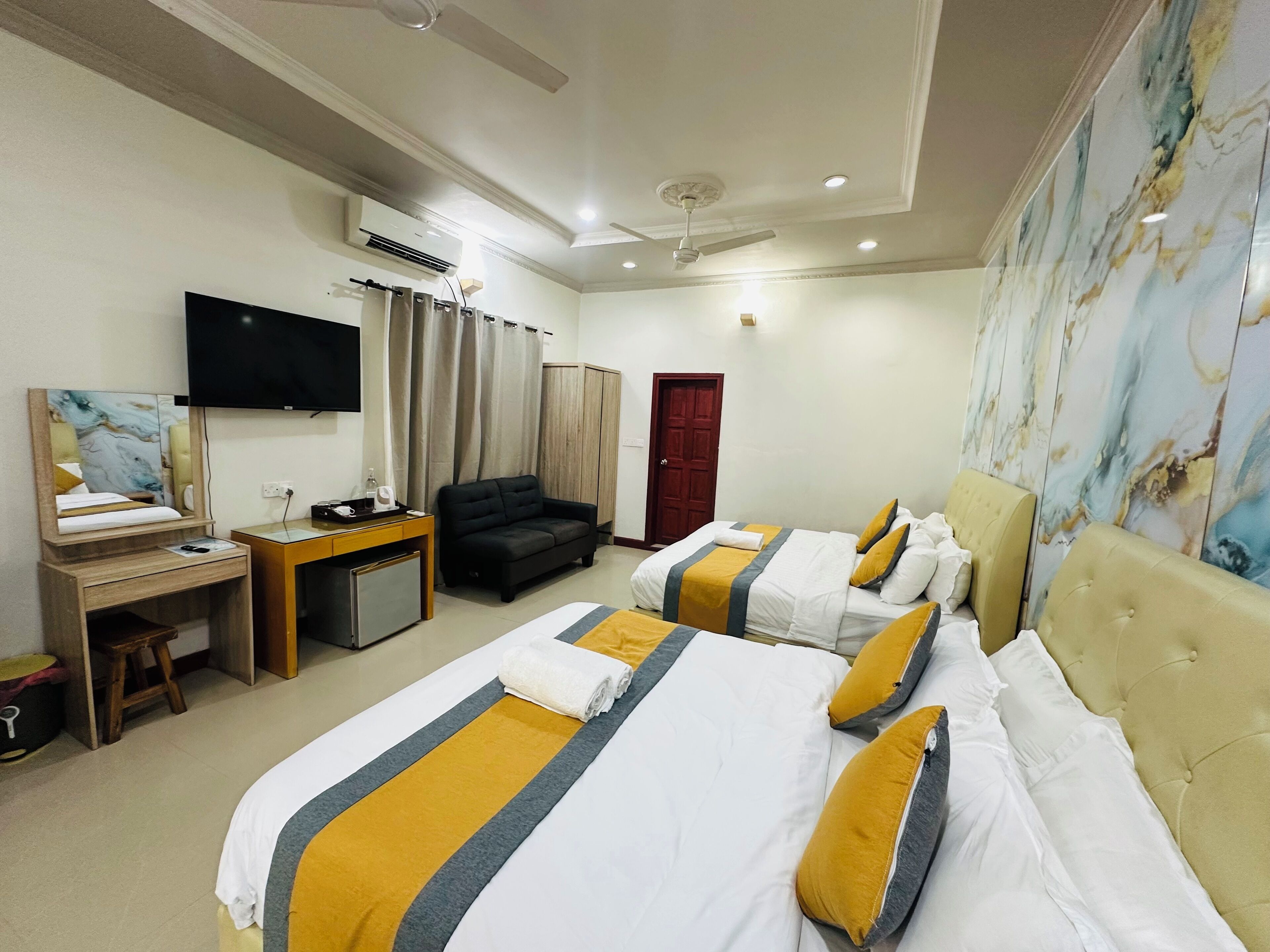 A hotel room with two beds, a desk, a TV, an air conditioner, and a red door.