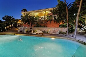 A pool area with lounge chairs and a hot tub, surrounded by palm trees and a building with a balcony. - Las Quintas Reserve  (Culebra)