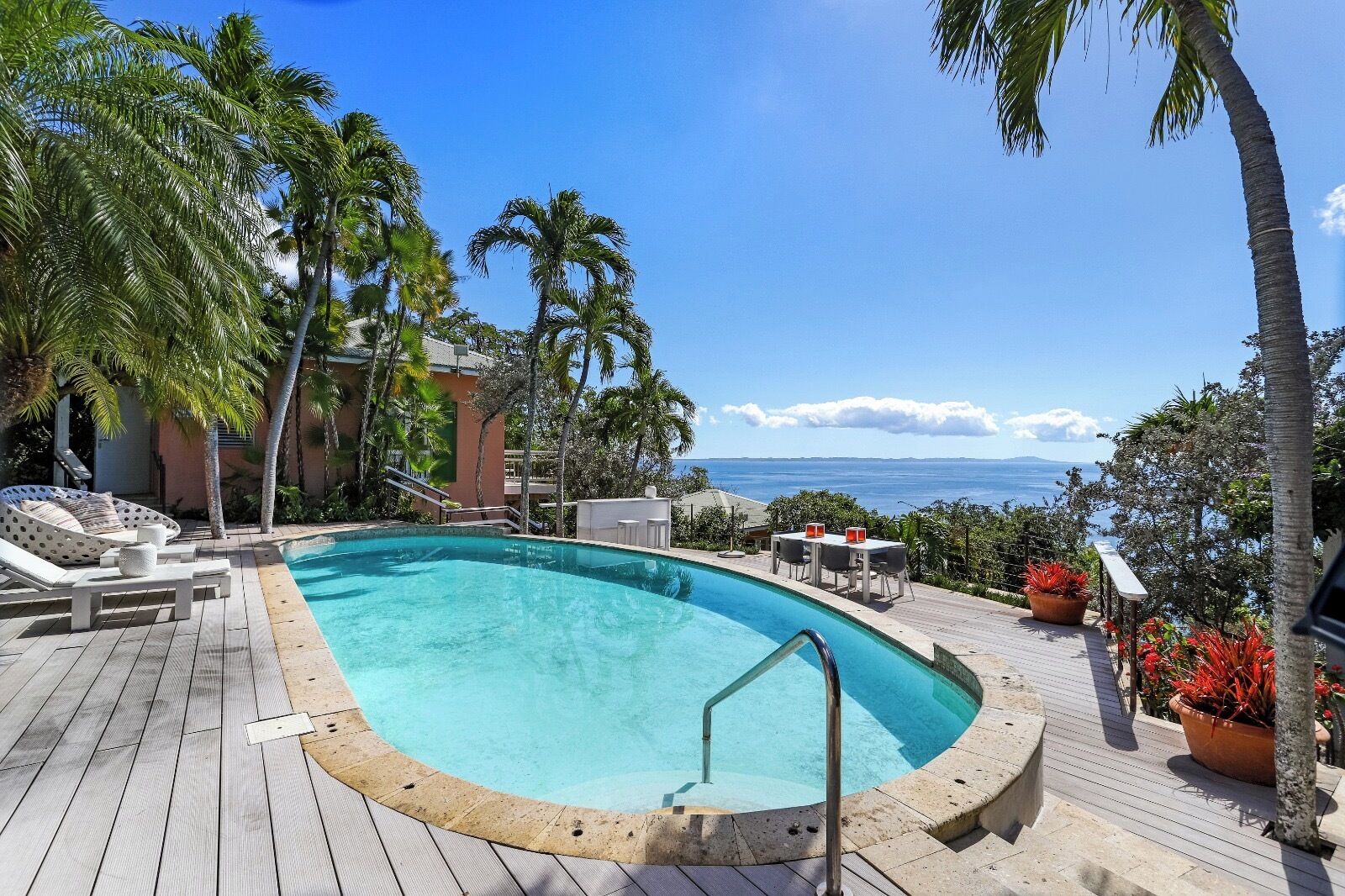 Ein Poolbereich mit Liegestühlen, einem Tisch und Blick aufs Meer.