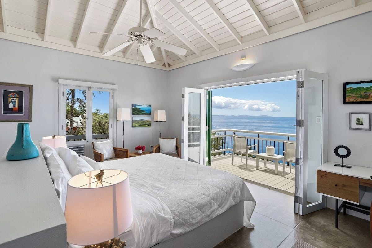 Un dormitorio con una cama grande, ventilador de techo y balcón con vista al mar.