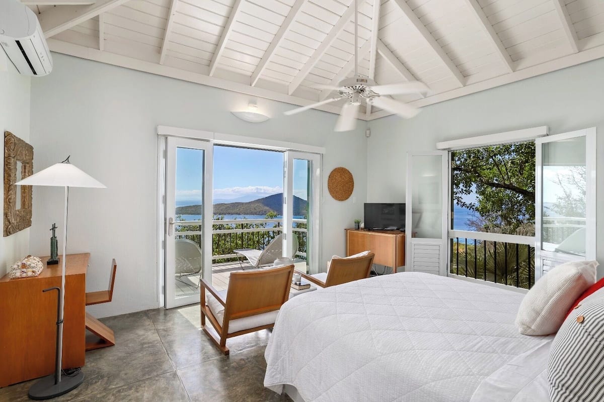 Un dormitorio con cama, escritorio, silla, televisor y balcón con vista al mar.