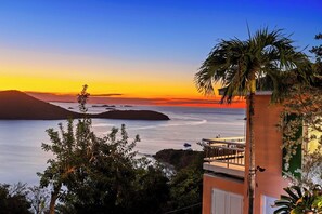 A coastal view with a sunset, a palm tree, and a building with a balcony overlooking the sea. - Las Quintas Reserve  (Culebra)