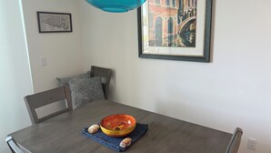 Une table à manger avec un saladier et des coquillages, une suspension bleue et un tableau encadré.