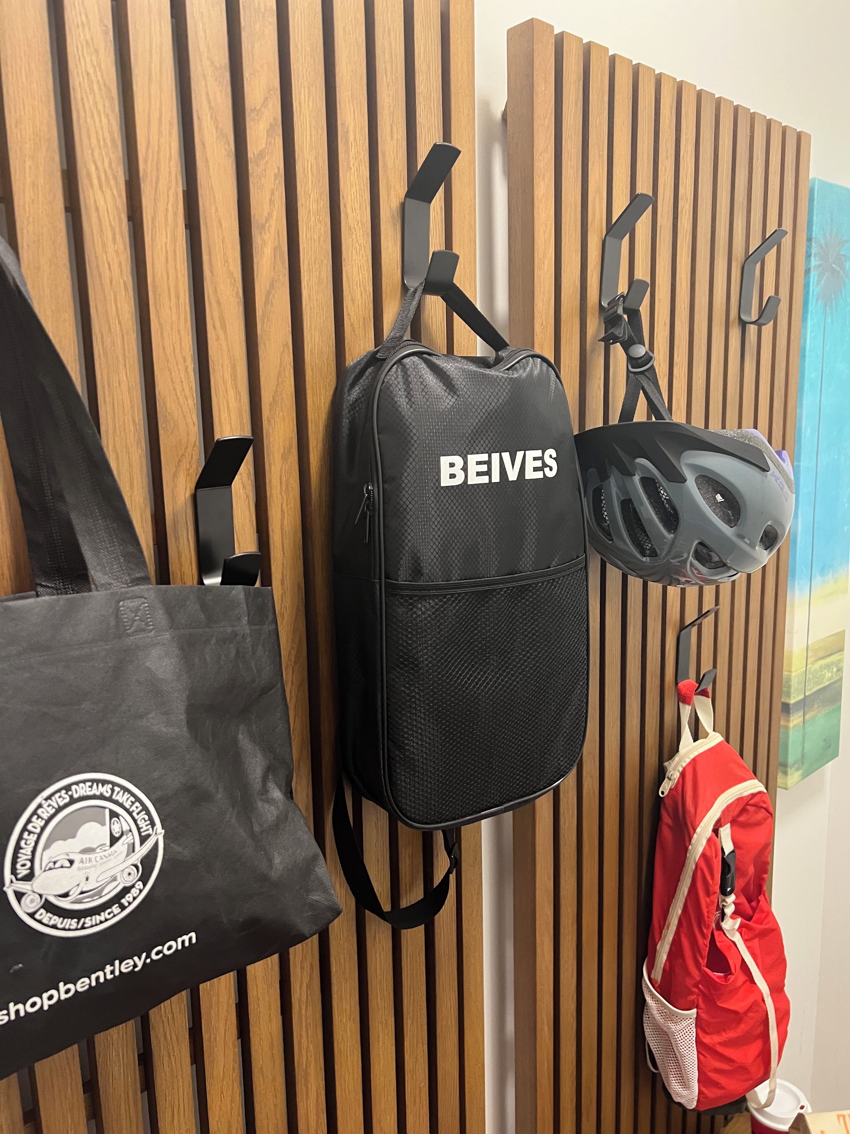 A black backpack with 'BEIVES' on it, a red bag, and a helmet hanging on a wooden wall.