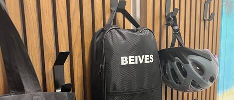 A black backpack with 'BEIVES' on it, a red bag, and a helmet hanging on a wooden wall.