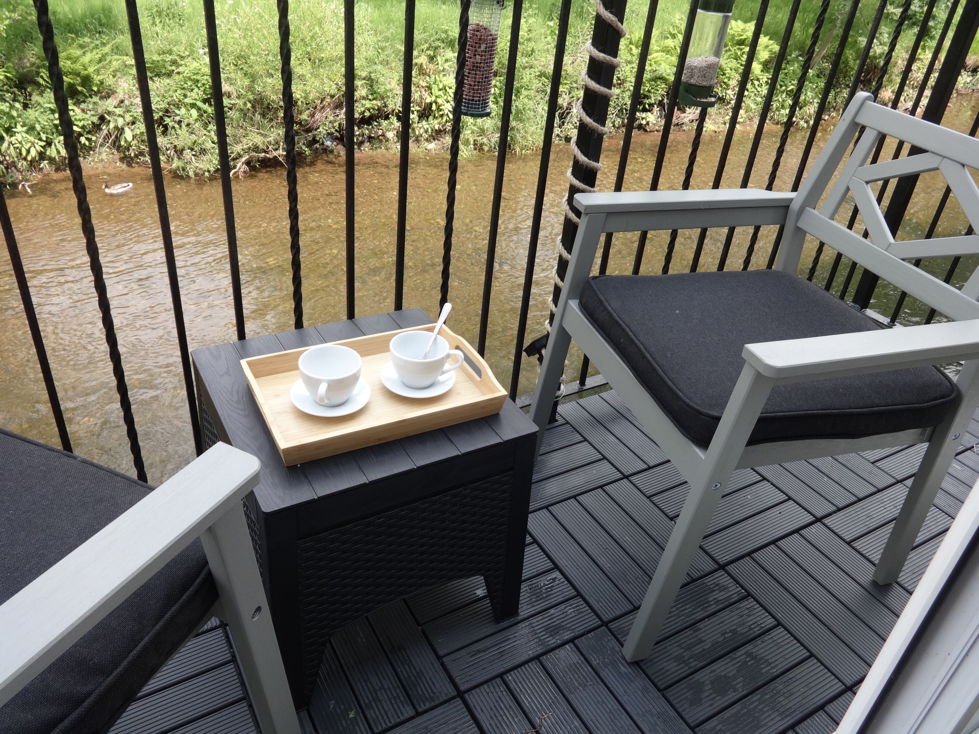 A deck with a chair and a small table holding two cups and a tray.