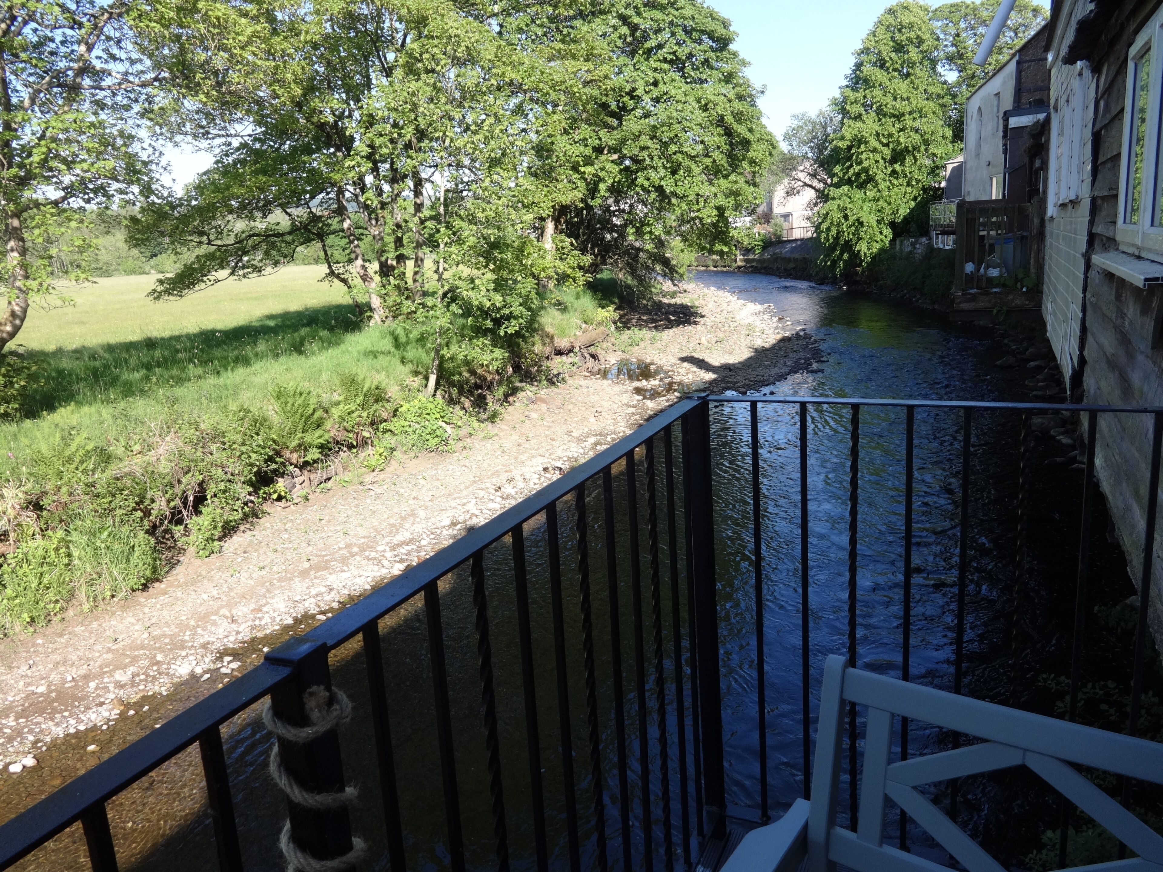 A river with a wooden bridge, surrounded by greenery and buildings.