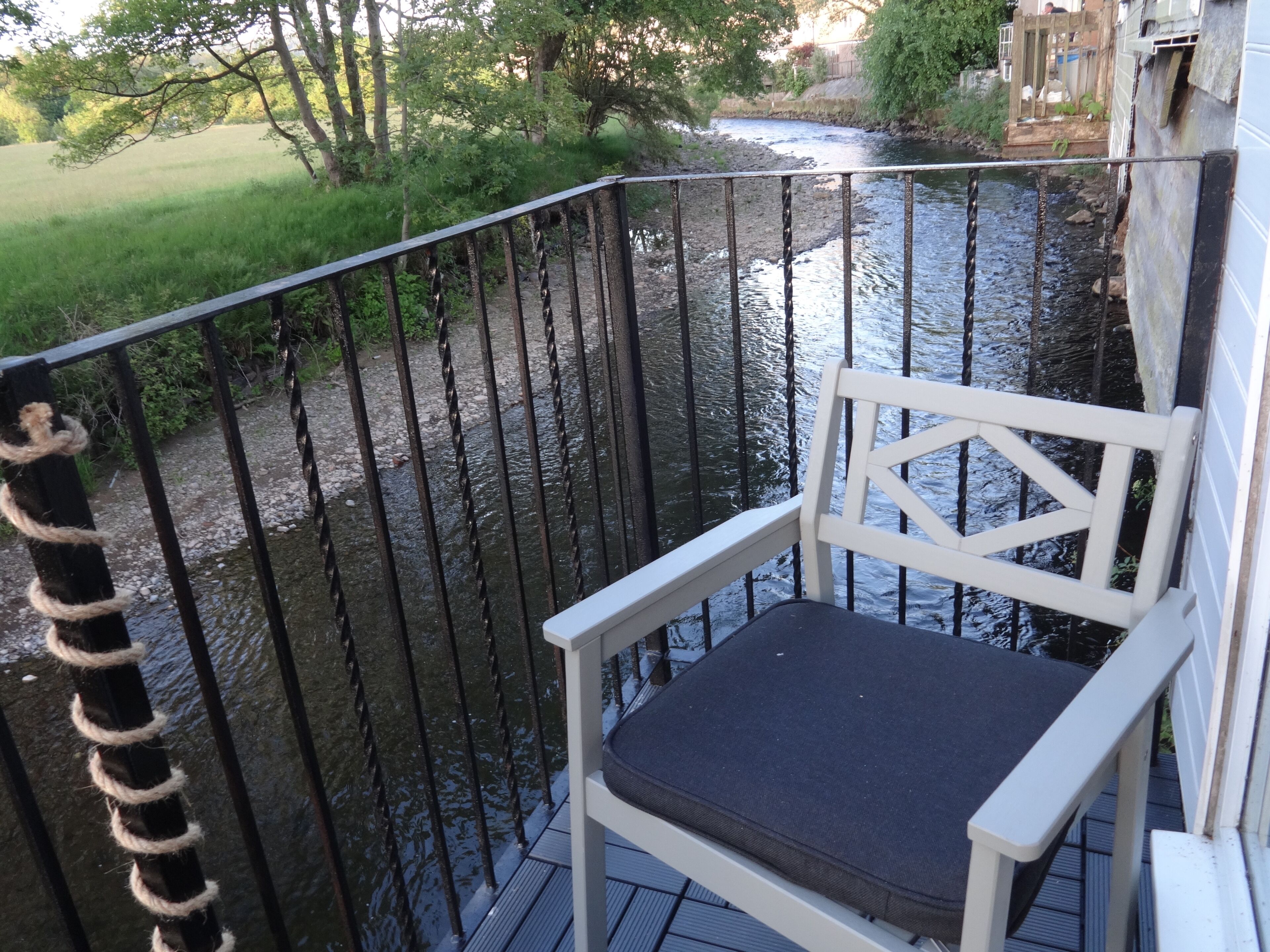 Een balkon met een witte stoel en een metalen reling, met uitzicht op een rivier.
