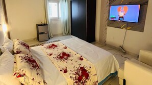 A hotel room with a bed, a TV mounted on the wall, a desk, and a wardrobe. - ROOM WITH INDOOR WELLNESS (Dakar)