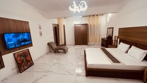 A modern bedroom with a large bed, a TV mounted on the wall, a chair, and a wardrobe. - ROOM WITH INDOOR WELLNESS (Dakar)
