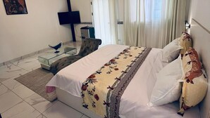 A hotel room with a bed, a desk, a chair, a flat-screen TV, and a painting on the wall. - ROOM WITH INDOOR WELLNESS (Dakar)