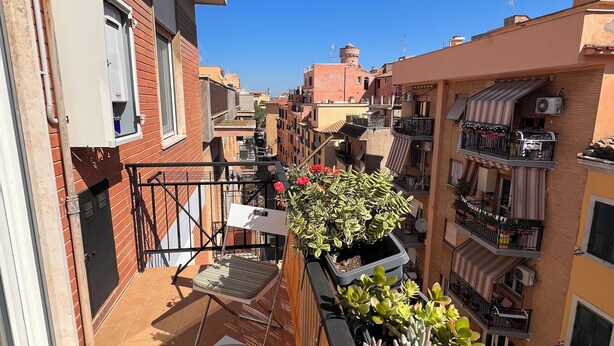 A narrow balcony with potted plants, a chair, and a small table.