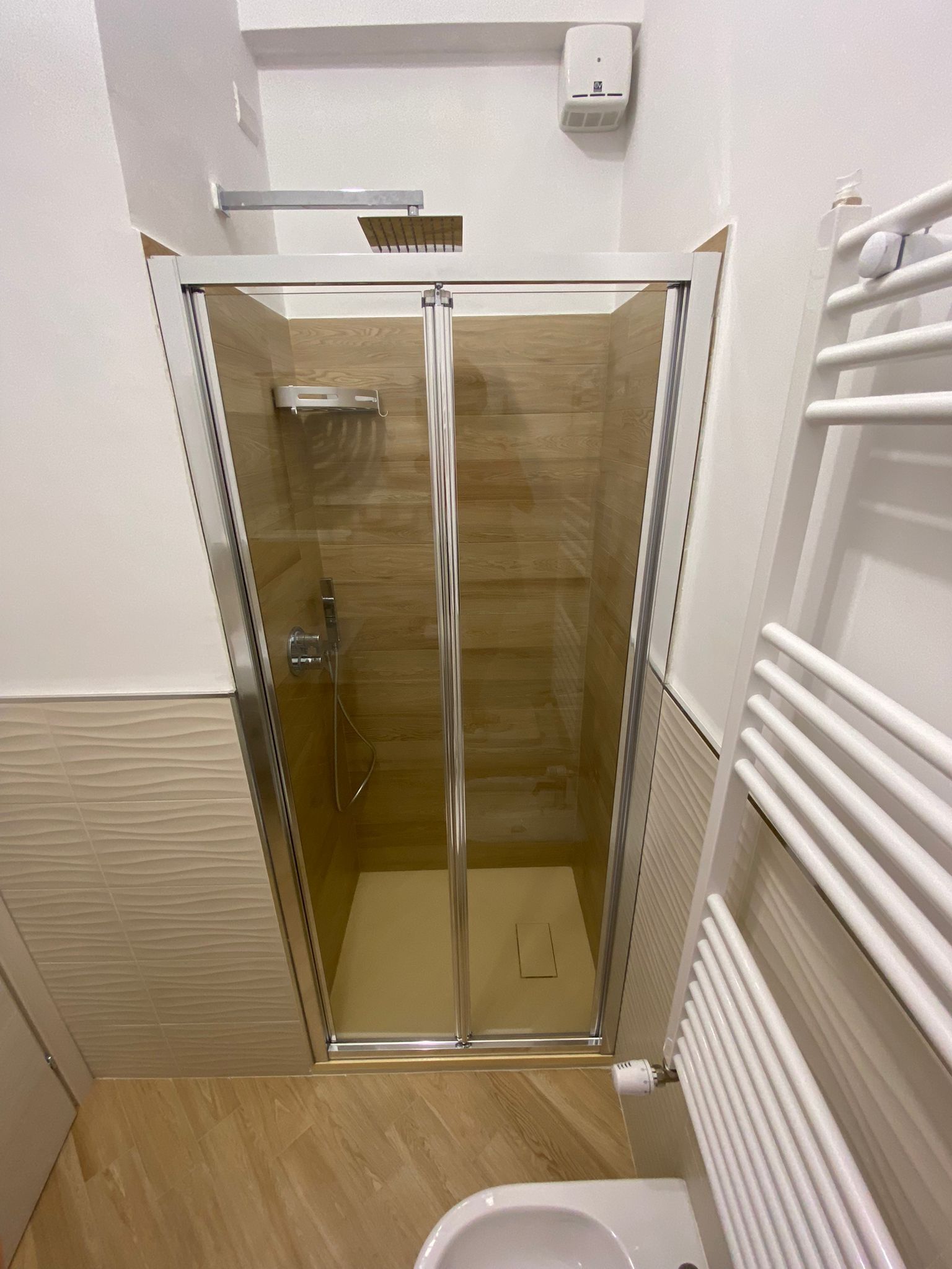 A glass-enclosed shower stall with a white towel rack and a soap dispenser on the wall.