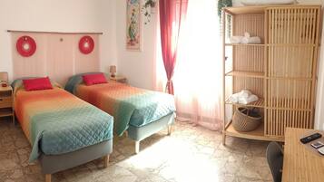 Ein Zimmer mit zwei Betten, einem Holzbodenregal mit Handtüchern, einem Tisch mit einer Fernbedienung und einem Fliesenboden.