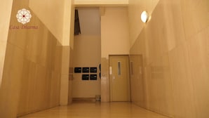 A hallway with a door at the end, a small trash bin, and a wall-mounted light fixture.