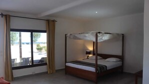 Una cama con dosel, una mesita de noche con lámpara, una ventana con cortinas y vistas al exterior.