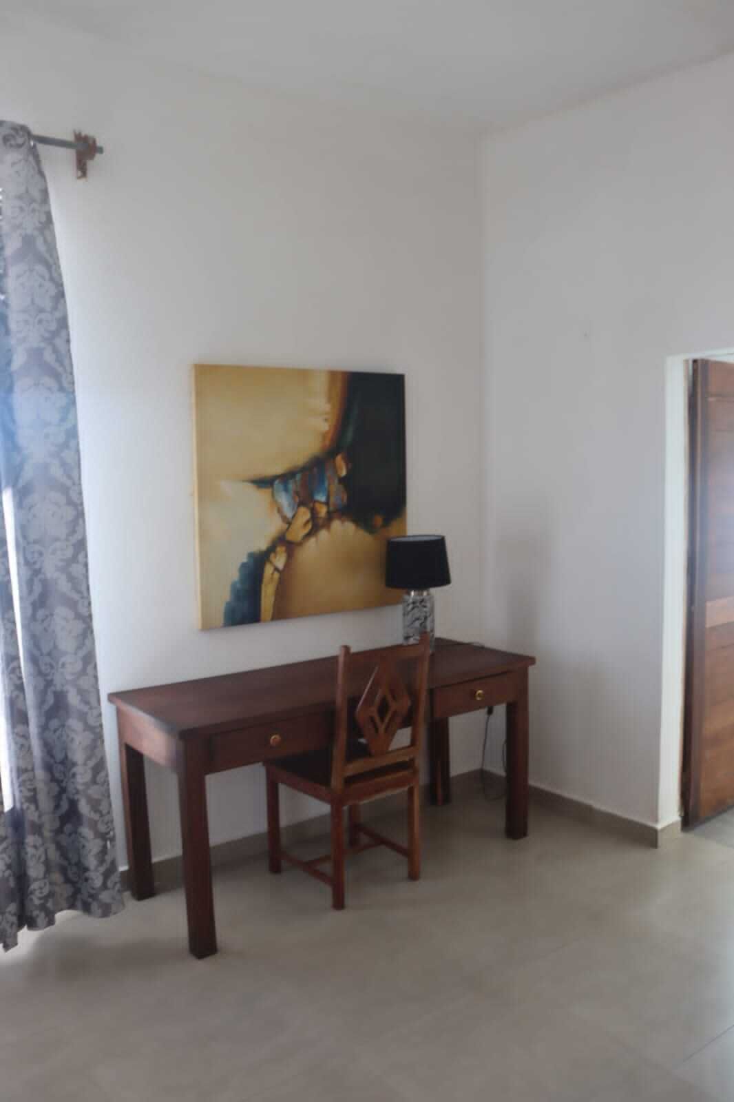 A room with a wooden desk, a chair, a lamp, and a painting on the wall.